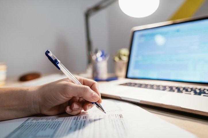 Dłoń z długopisem, faktura i laptop na biurku